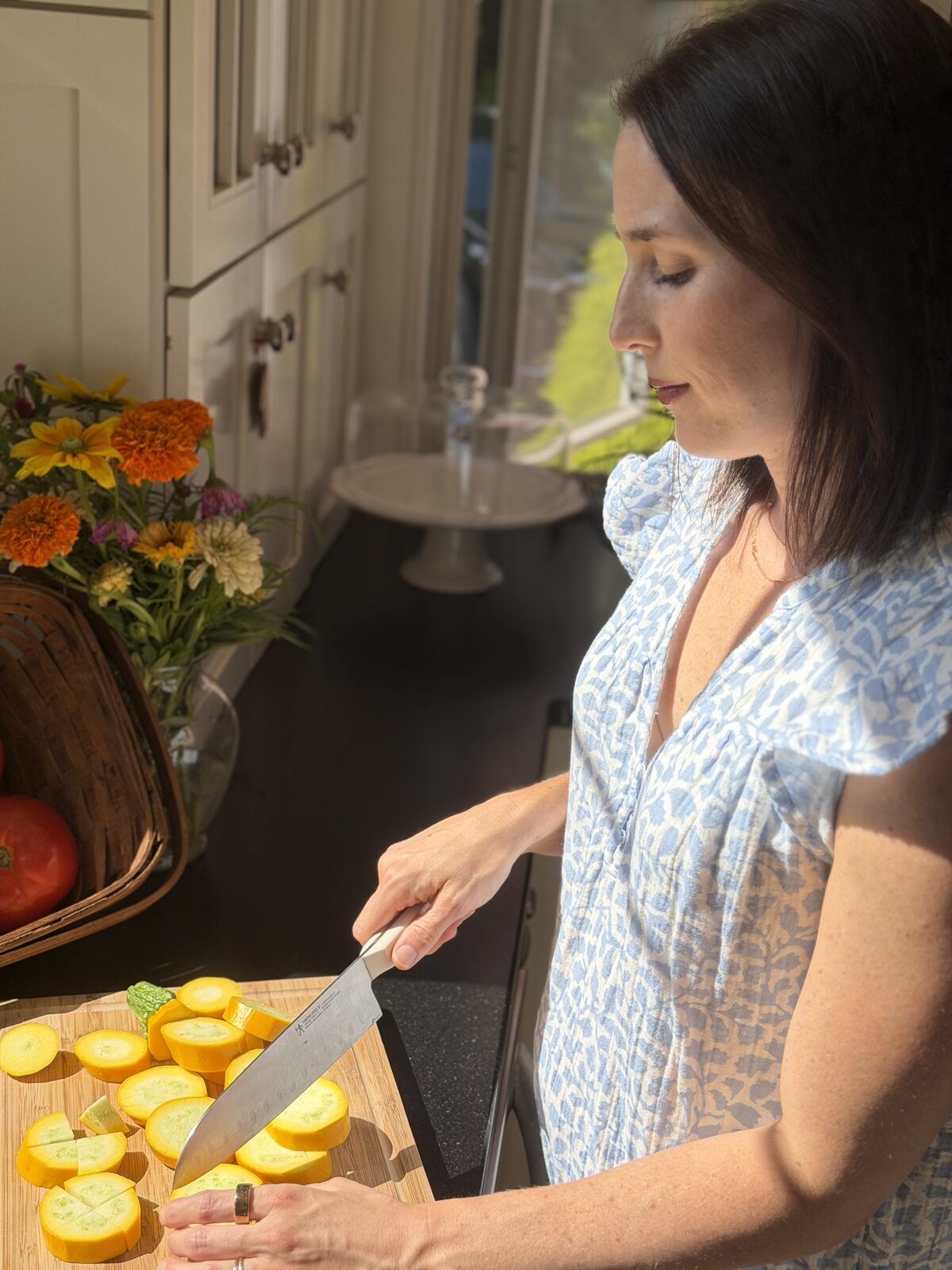Leigh slicing yellow summer squash on a wooden board in her sunlit kitchen