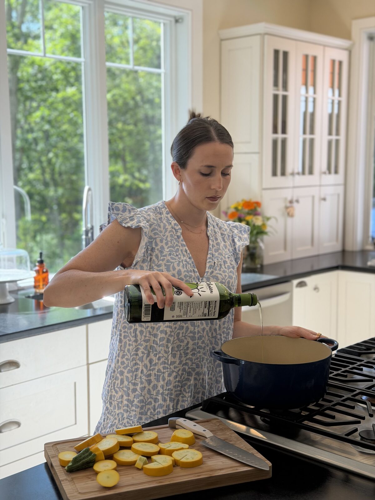 Leigh pouring olive oil into a pot beside a board of sliced summer squash