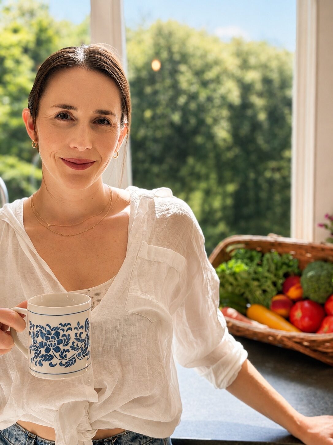 Leigh holding a mug in her kitchen beside a basket of fresh garden produce